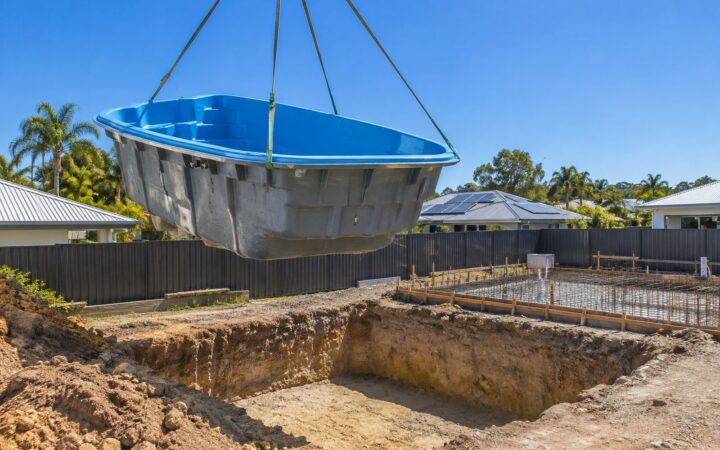 Blue fibreglass pool shell lifted by crane into an excavated hole on a Queensland building site